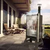 A smoker is set up on a patio with chairs and a table nearby, with food smoking inside the smoker. Produktbild-Vorschau