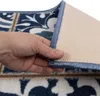 A hand is shown lifting the edge of a rug to reveal its backing. Produktbild-Vorschau