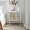A white nightstand with wood grain drawers next to a bed. Produktbild-Vorschau