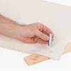A hand holding a metal tool over a piece of fabric with a pre-made hole, with a wooden block underneath. Produktbild-Vorschau