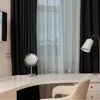 A vanity table with a mirror and a lamp, set against black and sheer curtains. Produktbild-Vorschau