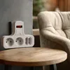 A white power strip with a red switch is mounted on a gray wall next to a wooden table and a beige armchair. Produktbild-Vorschau