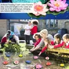 Children and adults interacting with artificial lotus flowers floating in a pond. Produktbild-Vorschau