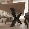 A close-up view of a dining table with a distinctive X-shaped metal base, surrounded by chairs in a dining room setting. Produktbild-Vorschau
