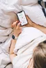 A person lying in bed, holding a smartphone and wearing a smartwatch. Náhľad obrázku produktu