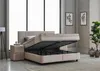 A beige boxspring bed with its mattress lifted to reveal storage space underneath, set in a modern bedroom with decorative plants and artwork. Produktbild-Vorschau