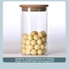 A clear glass jar filled with small, round, light-colored objects, topped with a wooden lid. Produktbild-Vorschau
