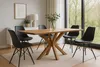 A dining table with chairs in a well-lit room with a large window overlooking greenery. Produktbild-Vorschau