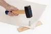 A hand holding a sledgehammer over a metal punch and a piece of fabric, with wooden wedges underneath. Produktbild-Vorschau