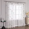 A close-up view of sheer curtains with a floral pattern hanging in front of a window. Produktbild-Vorschau