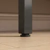 Close-up of the base of a black metal furniture leg resting on a light wood floor, with a beige baseboard in the background. Anteprima dell’immagine prodotto