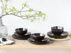 A set of dark brown ceramic dishes arranged on a wooden surface, with a vase and branches in the background. Náhľad obrázku produktu