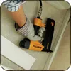 A person wearing a glove is using a pneumatic nail gun to attach a piece of trim. Podgląd zdjęcia produktu