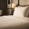 A close-up view of a neatly made hotel bed with white striped bedding and a pillow. Produktbild-Vorschau