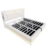A white upholstered bed frame with a metal slatted base, shown from a diagonal angle against a white background. The bed has a headboard with integrated LED lighting and side storage compartments. Náhľad obrázku produktu