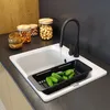 A kitchen sink with a faucet running water into a colander filled with cucumbers. Jars of nuts and wooden bowls are on the counter. Podgląd zdjęcia produktu