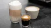 Three coffee drinks are displayed on a dark countertop. Produktbild-Vorschau