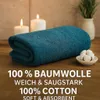 A folded teal towel is displayed on a wooden surface, with two lit candles and a small bowl of cotton balls in the background. Produktbild-Vorschau
