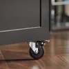 A close-up shot of a black cabinet with a caster wheel and brake. Produktbild-Vorschau