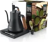 A black electric kettle with a wood-grain handle sits on its charging base, next to its packaging which features images of matcha tea. Náhled obrázku produktu