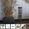 A black solar-powered garden light with a decorative pattern stands next to a large potted plant with dry grass. Produktbild-Vorschau