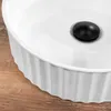 A close-up view of a white ceramic sink with a black drain cover, resting on a wooden surface. Produktbild-Vorschau
