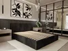 A modern bedroom with a dark upholstered bed frame and slatted base, flanked by nightstands. Abstract art hangs on the wall, and a large mirror reflects the room. Produktbild-Vorschau