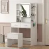 A white dressing table with a mirror, drawers, and shelves, along with a matching stool. The setup is in a room with a neutral wall and door. Náhled obrázku produktu