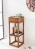A wooden side table with a drawer and shelves, holding books and a vintage telephone. A large clock is visible on the wall in the background. Náhľad obrázku produktu
