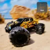 A remote-controlled monster truck driving on a sandy beach with a blurred background of rocks and the ocean. Voir les images du produit
