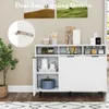 A white kitchen sideboard with various items on display, including jars, pitchers, and a pot. There are also two framed landscape pictures on the wall behind it. Produktbild-Vorschau