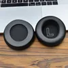 Two black headphone ear pads are placed on a wooden surface in front of a laptop keyboard. Podgląd zdjęcia produktu