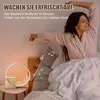A woman waking up in bed, stretching, with a sunrise alarm clock on the nightstand. Produktbild-Vorschau
