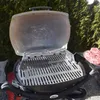 A Weber grill with raw meat on a plate next to it, outdoors with trees in the background. Náhľad obrázku produktu
