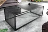 A modern coffee table with a black metal frame and a graphite glass top, placed on a concrete floor in a living room setting. Produktbild-Vorschau