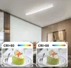A modern white LED ceiling light fixture is shown installed on a white ceiling in an office or living space. Below the fixture, two identical images of a green cake with fruit topping are displayed, each with a "CRI>80" label and a color spectrum bar. Podgląd zdjęcia produktu