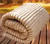 A folded blanket with a ribbed texture is placed on a wooden surface, with a blurred background of autumn foliage. Produktbild-Vorschau