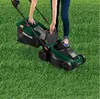 A person is using a green electric lawnmower on a grassy lawn. Produktbild-Vorschau