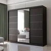 A modern sliding door wardrobe with a mirrored front panel, set in a well-lit room with green curtains and a glimpse of a sofa and stool reflected in the mirror. Produktbild-Vorschau