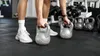 A person's legs and hands are shown in a gym setting, reaching for a kettlebell. Náhľad obrázku produktu