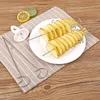 A potato spiralizer tool and spiralized potatoes on skewers are displayed on a striped cloth on a wooden table, with lemon and lime slices in the background. Náhled obrázku produktu