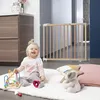A baby is playing on a rug in front of a wooden baby gate, with furniture in the background. Produktbild-Vorschau