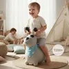 A young child is happily riding a gray inflatable dog toy in a playroom, with another child playing in the background and a teepee tent. Produktbild-Vorschau