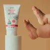A tube of sunscreen lotion is placed on a white pedestal next to a baby's feet. Anteprima dell’immagine prodotto