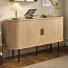 A modern wooden sideboard with black legs, featuring a ribbed texture and two black handles. It is placed in a room with a wooden floor and a beige rug. A lamp, a record player, and a bowl of fruit are on top of the sideboard. Anteprima dell’immagine prodotto