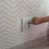A child's hand is shown pressing a button on a white electrical outlet cover, which is a type of childproofing device. Anteprima dell’immagine prodotto