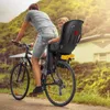 A person is riding a bicycle with a child in a seat behind them on a paved road with greenery and a house in the background. Náhled obrázku produktu