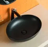 A black ceramic vessel sink with a chrome faucet is shown on a light wood countertop, with orange tiles in the background. Náhľad obrázku produktu