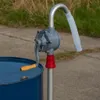 A rotary drum pump is shown attached to a blue barrel, with a grassy background. Náhľad obrázku produktu