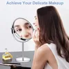 A woman is applying makeup in front of a vanity mirror, with a perfume bottle and makeup brushes on the vanity. Produktbild-Vorschau